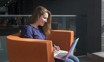 艾弗里坐在高级技术中心的一张橙色椅子上，在她的笔记本电脑上工作. 阳光透过窗户照进来.