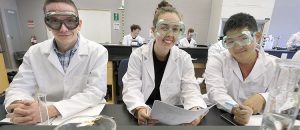 Three medical students wearing safety goggles and posing in a medical lab