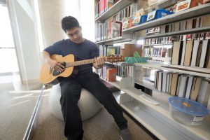 Jacky Wu playing the guitar at the library at LU's Orillia Campus