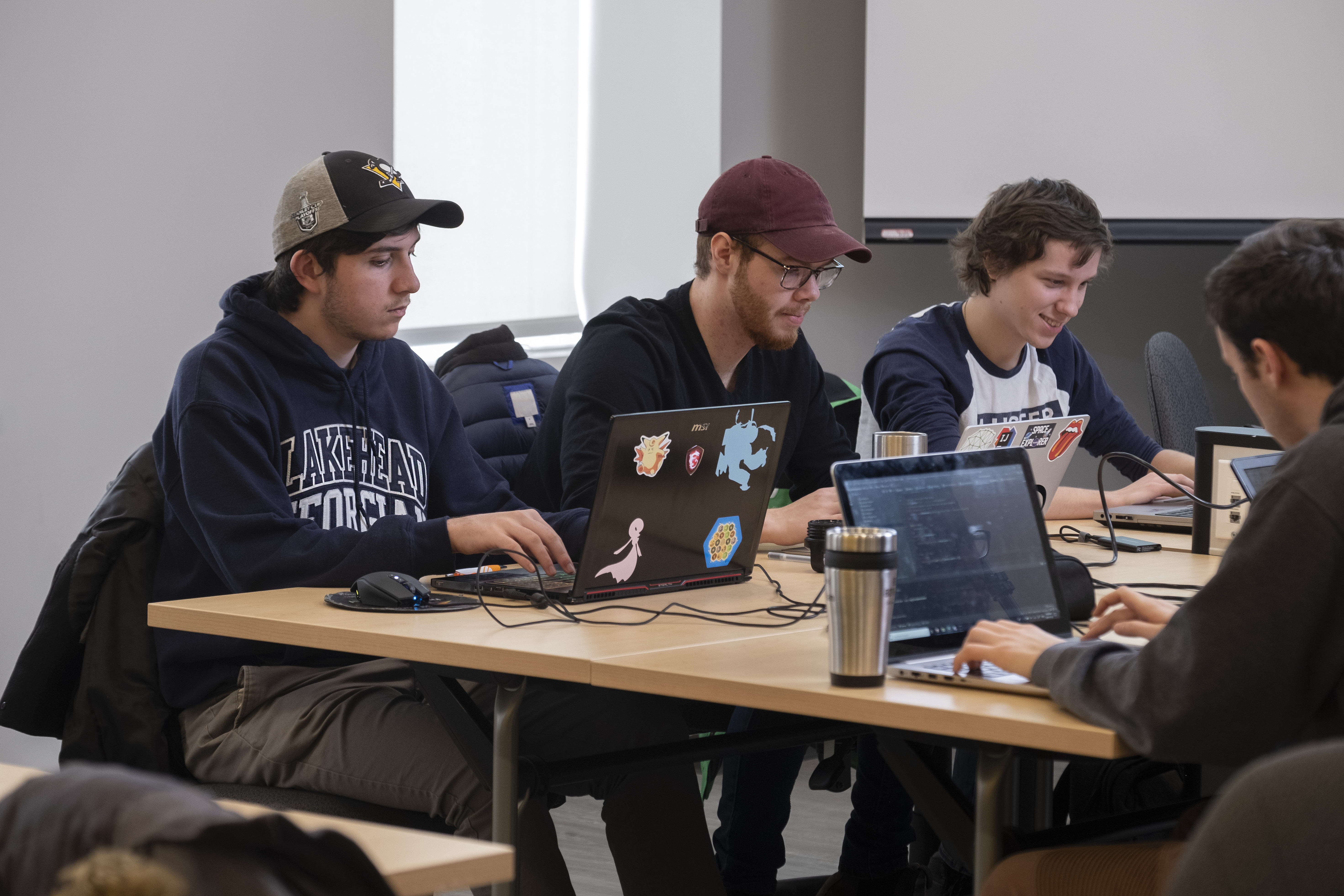 Three male students work on their laptops in computer science class